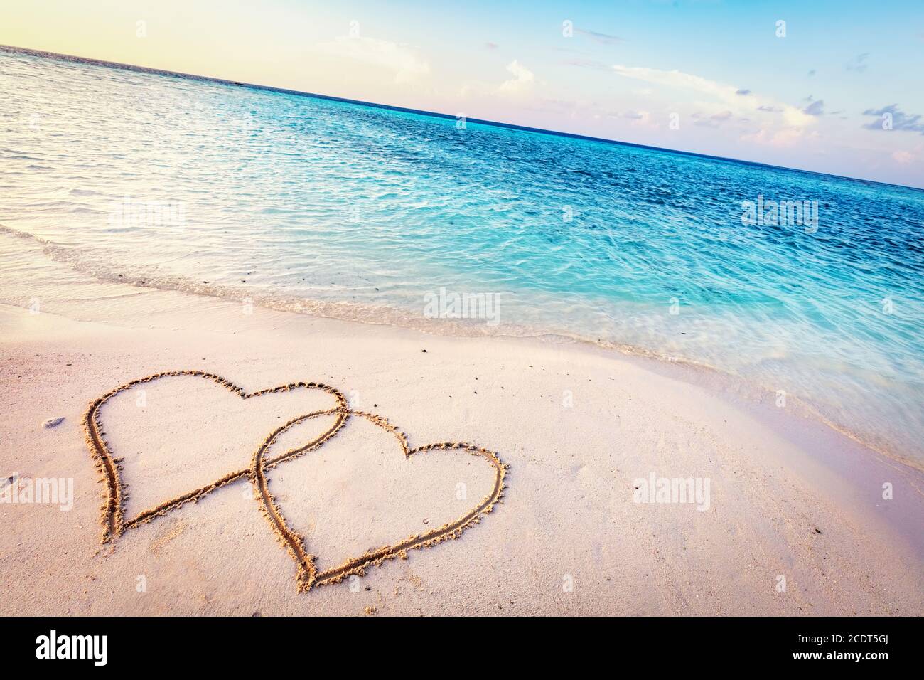 Two hearts drawn on sand of a tropical beach at sunset. Stock Photo
