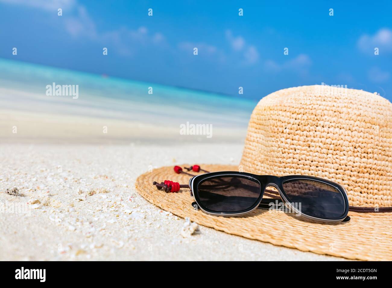 Sun hat and sunglasses on sand, clear turquoise ocean in Maldives. Stock Photo