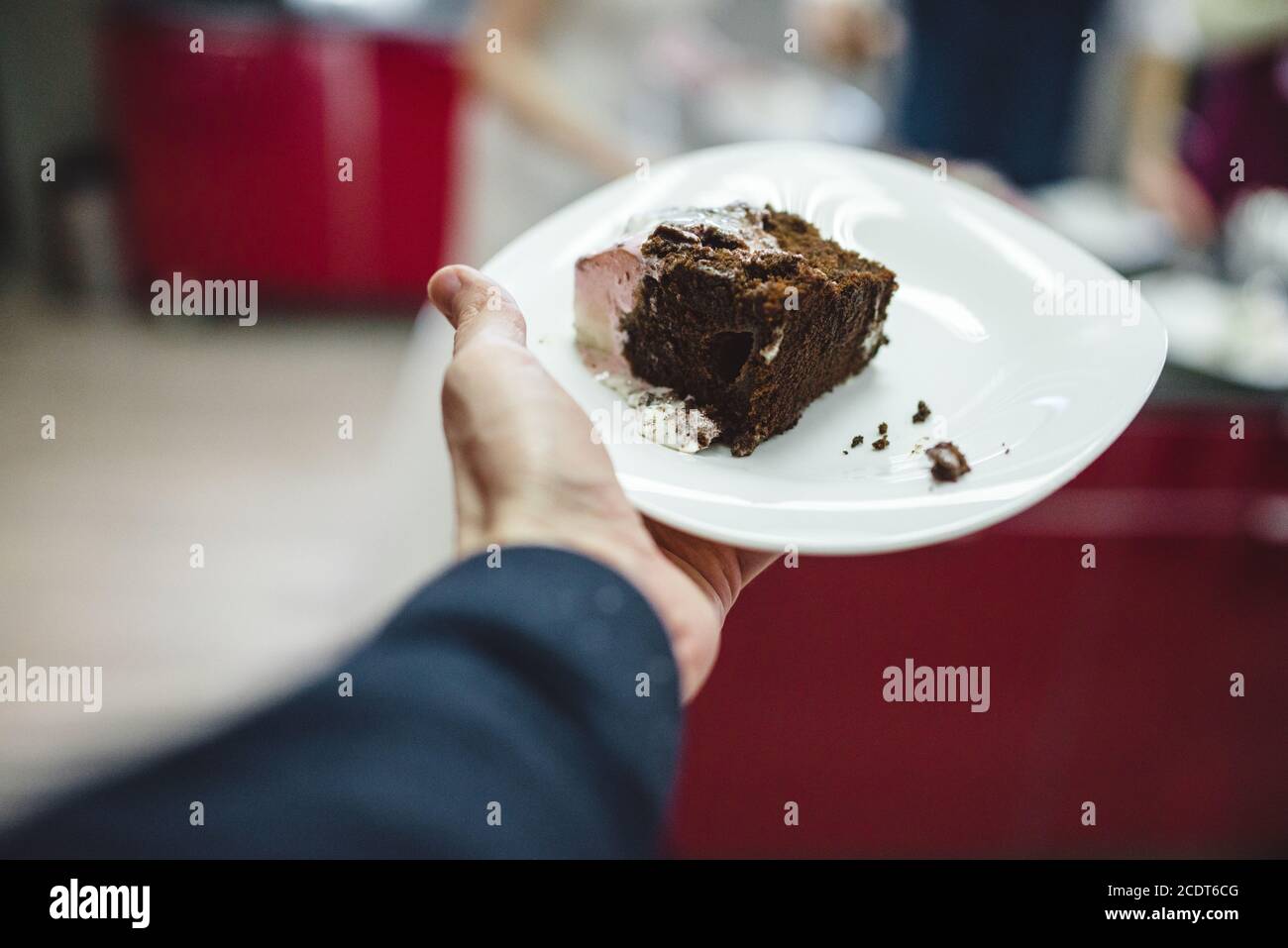 men's hand holding Slice of glazed chocolate wedding cake on the plate Stock Photo
