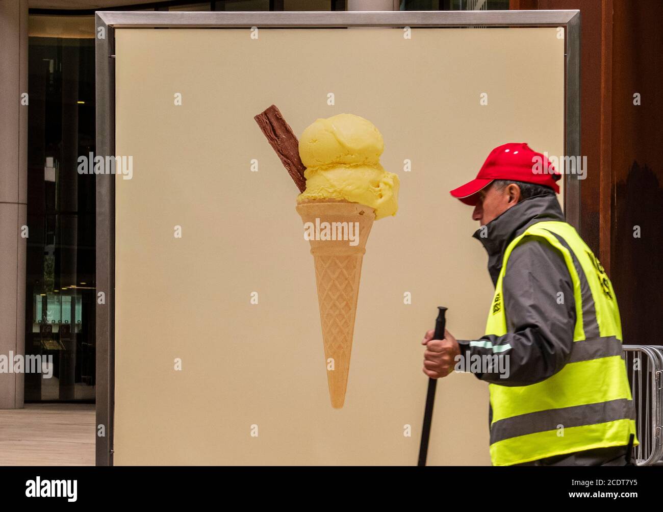 Man wearing high vis vest working by poster with ice cream cone, Kings Cross, London, England Stock Photo
