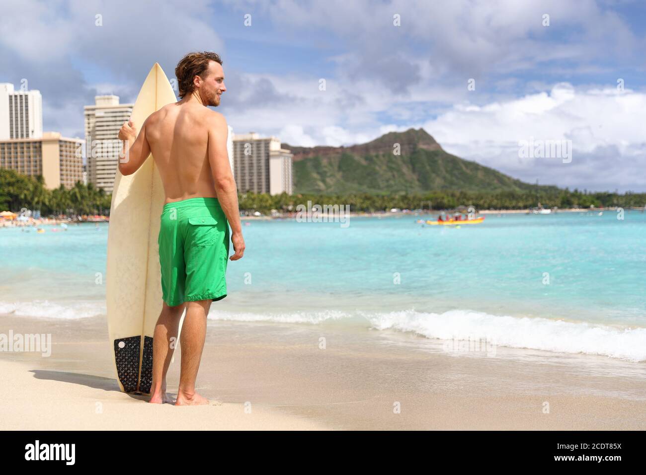 Hawaii surf man surfer surfing on Waikiki beach. Athlete standing with surfboard looking at ocean water, diamond head mountain in the landscape Stock Photo