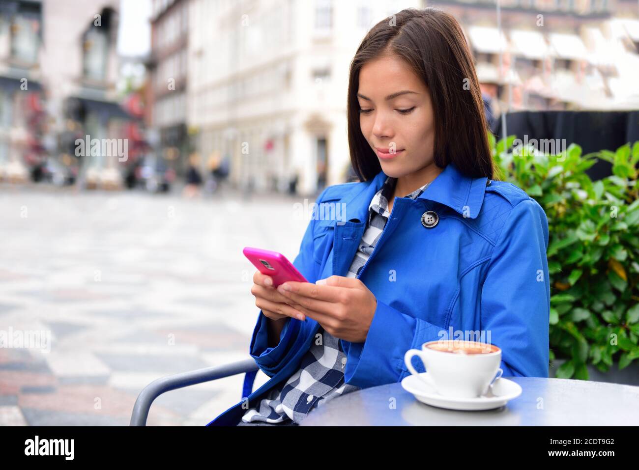 Cafe woman texting sms on phone app drinking cappuccino coffee at outdoor street terrasse in european city. Europe travel lifestyle. Asian Stock Photo