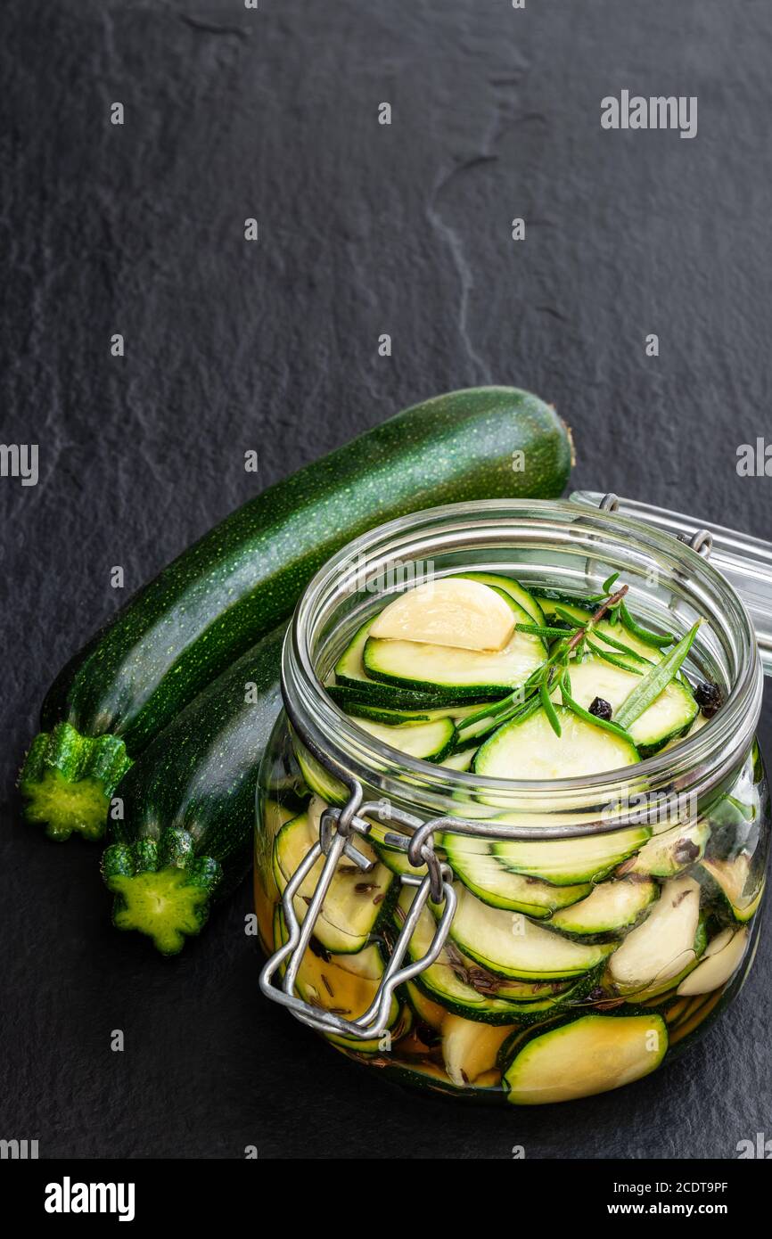 Marinated  zucchini slices in glass jar on black stone background Stock Photo