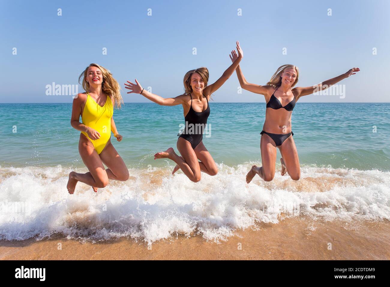 Three girls jumping on beach near sea Stock Photo