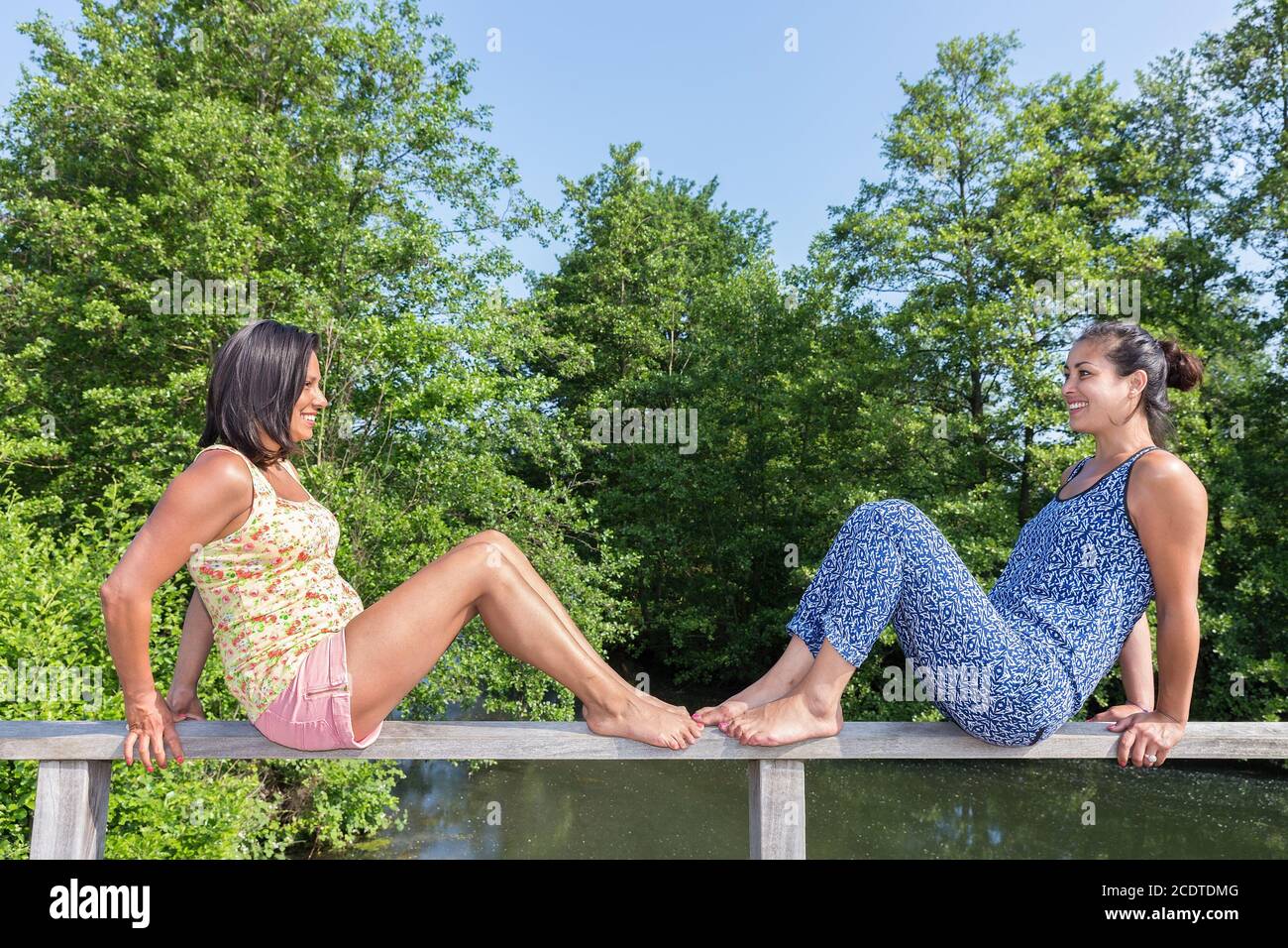 Two women sitting opposite on bridge railing Stock Photo