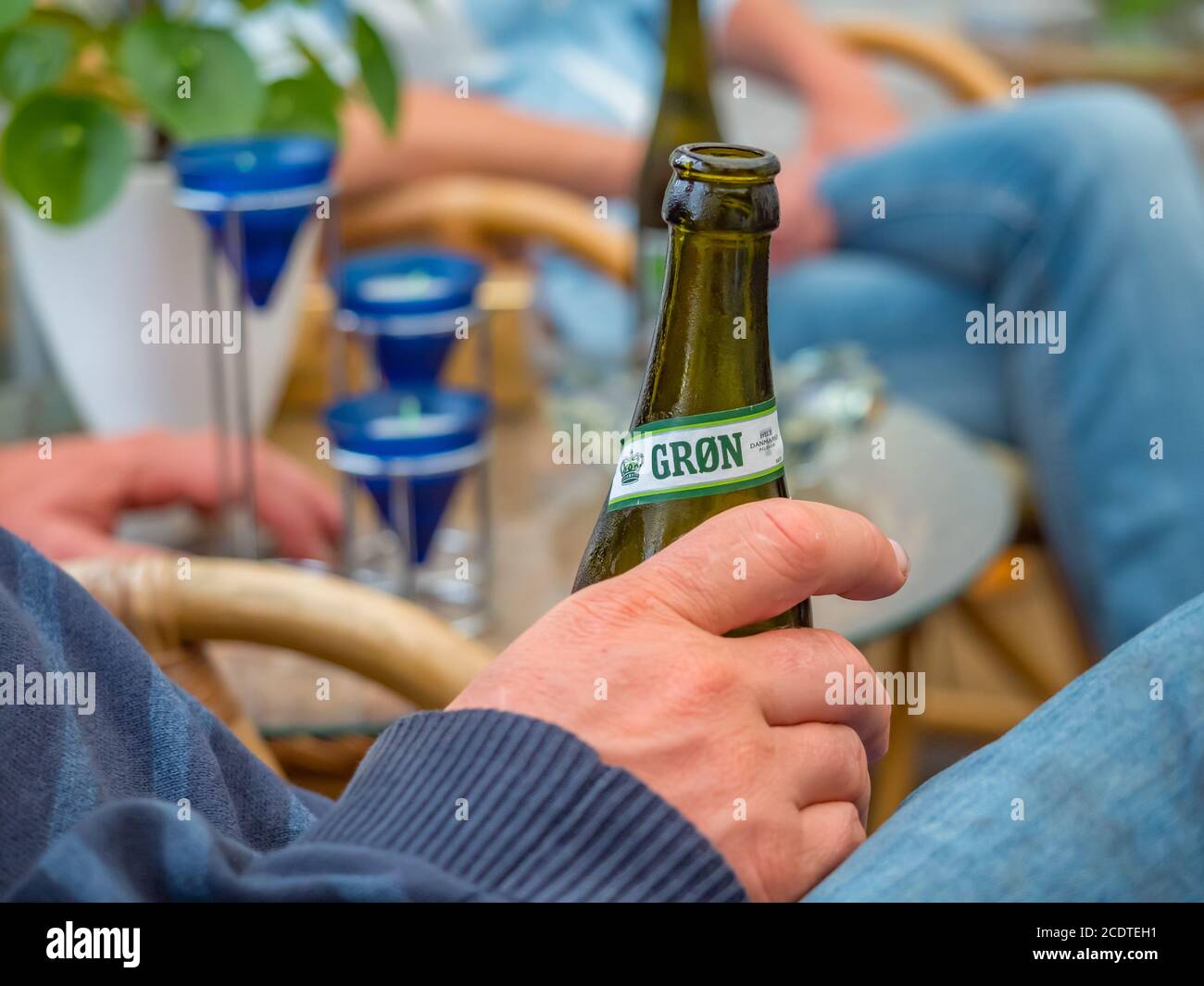 A guy holding a cold Tuborg Beer bottle sitting on a rattan chair on a cloudy summer afternoon Stock Photo