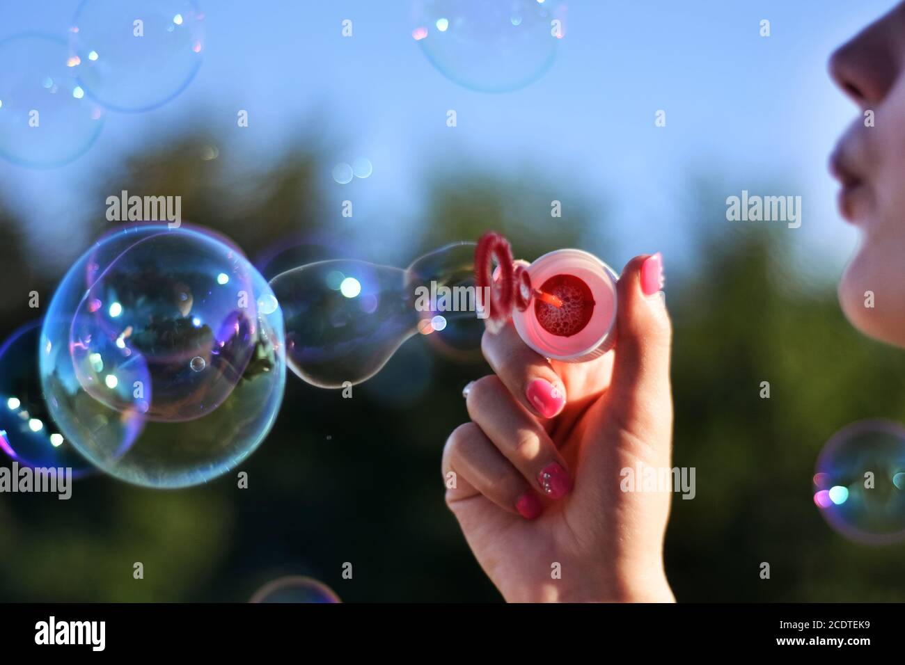 Young woman blowing soap bubbles outdoor in the park on summer sunset. Girl holding tool for bubbles in hand. Happiness in nature concept Stock Photo