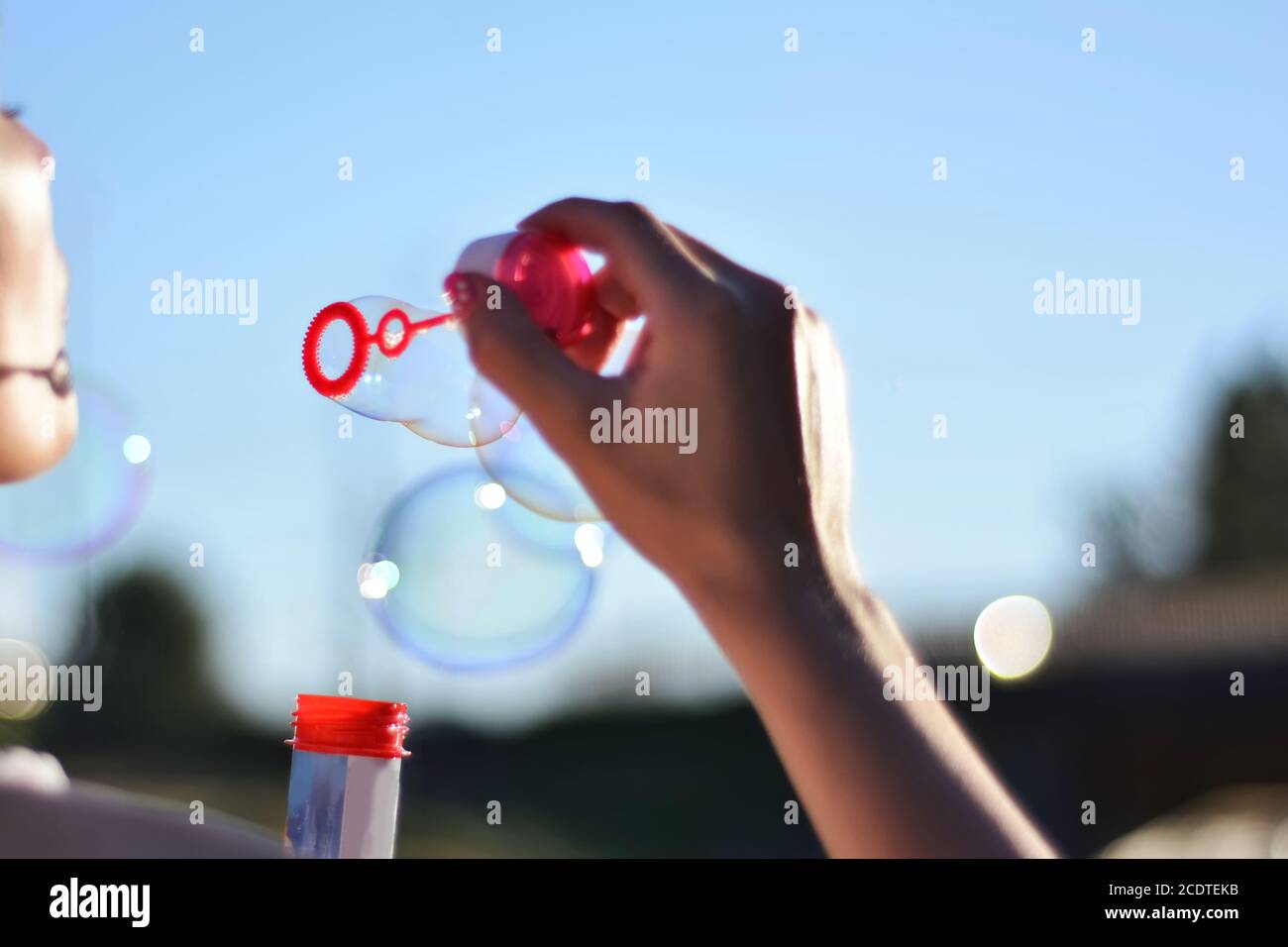 Young woman blowing soap bubbles outdoor in the park on summer sunset. Happiness in nature concept. Close up, selective focus Stock Photo