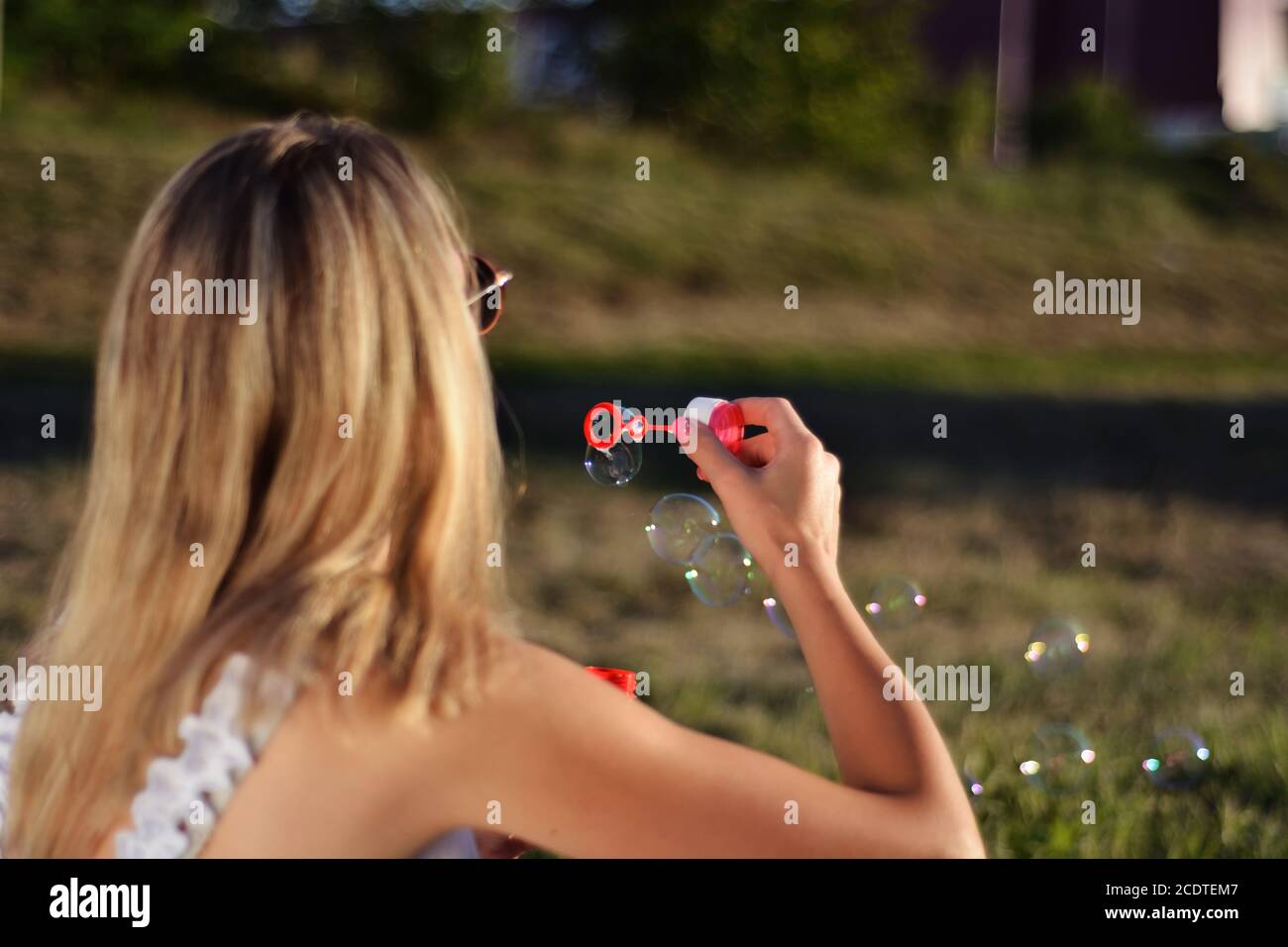 Blonde woman blowing soap bubbles outdoor in park on summer sunset. Happiness in nature concept. Close up, selective focus Stock Photo