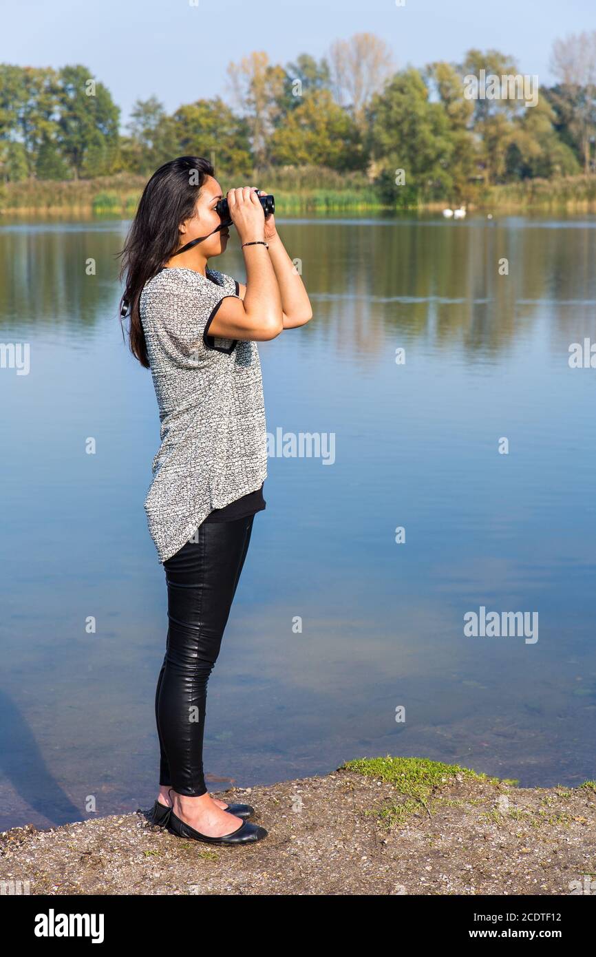 Woman looking through binoculars at water Stock Photo