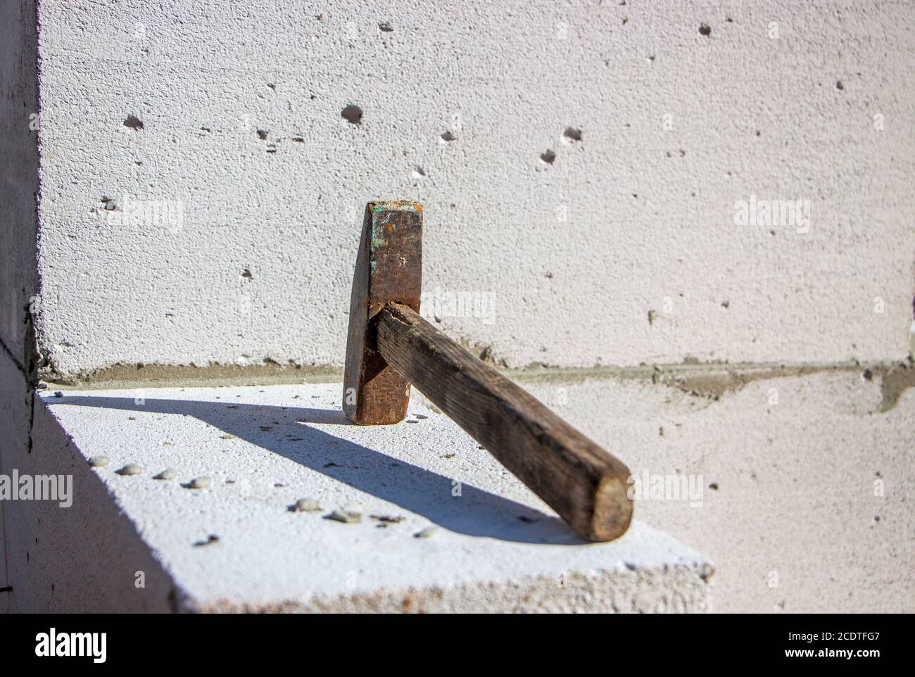 An old hammer on a white foam concrete block from which to build a house from which the shadow falls Stock Photo