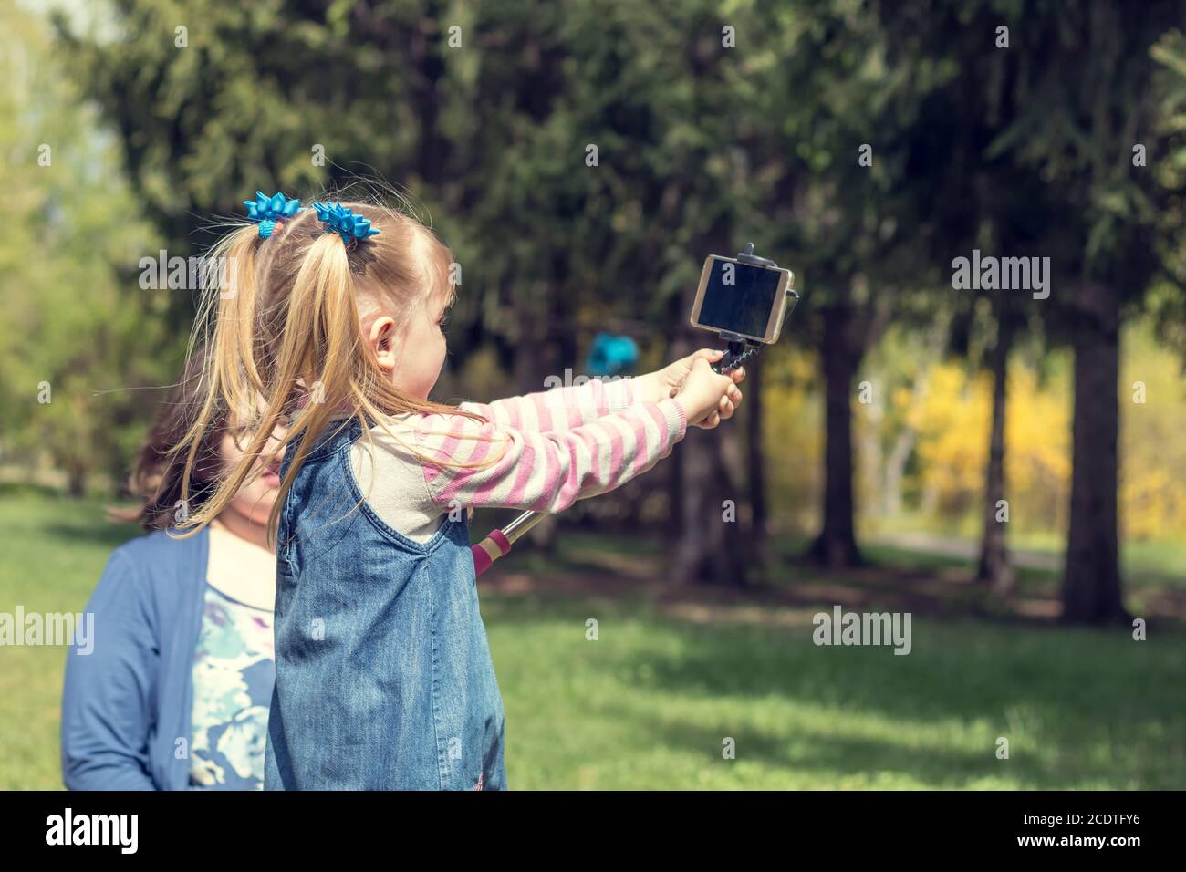 Cute little blonde girl with two ponytails taking selfie in the city park on a spring sunny day Stock Photo