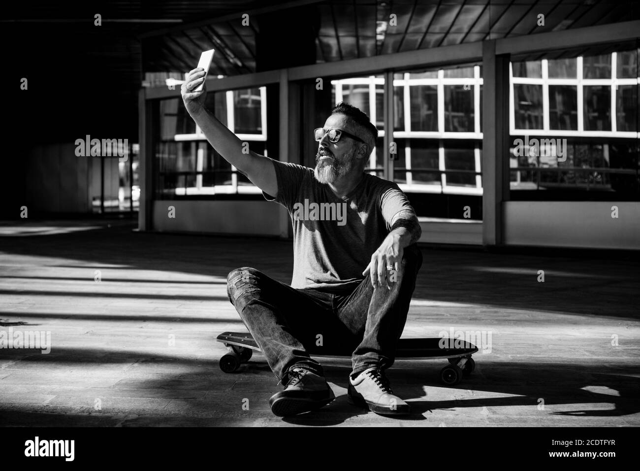 Black and white image of skater taking a selfi on a skateboard Stock Photo