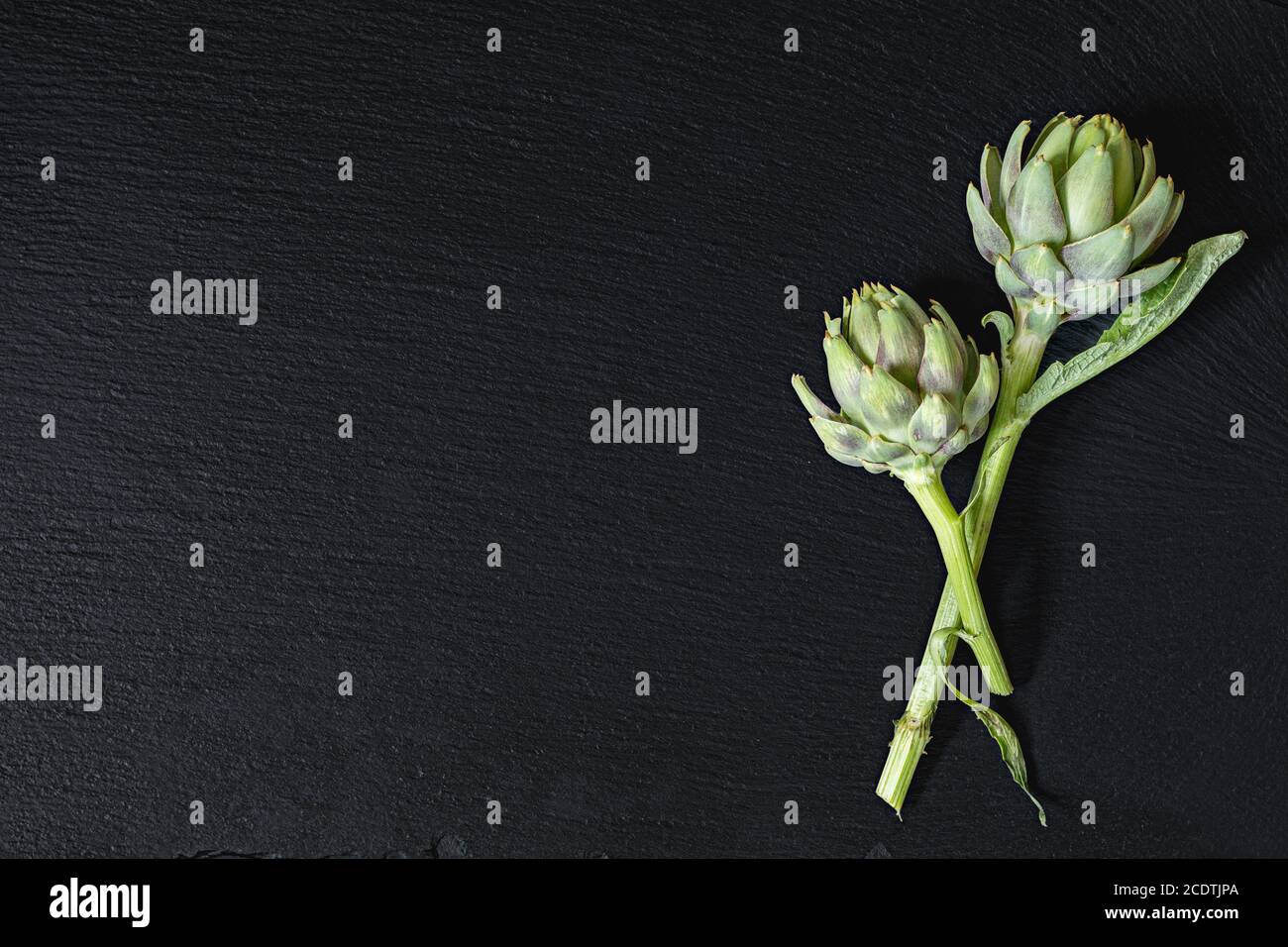Two cones fresh green artichoke on a black stone surface.  Top view, copy space. Healthy eating concept. Stock Photo