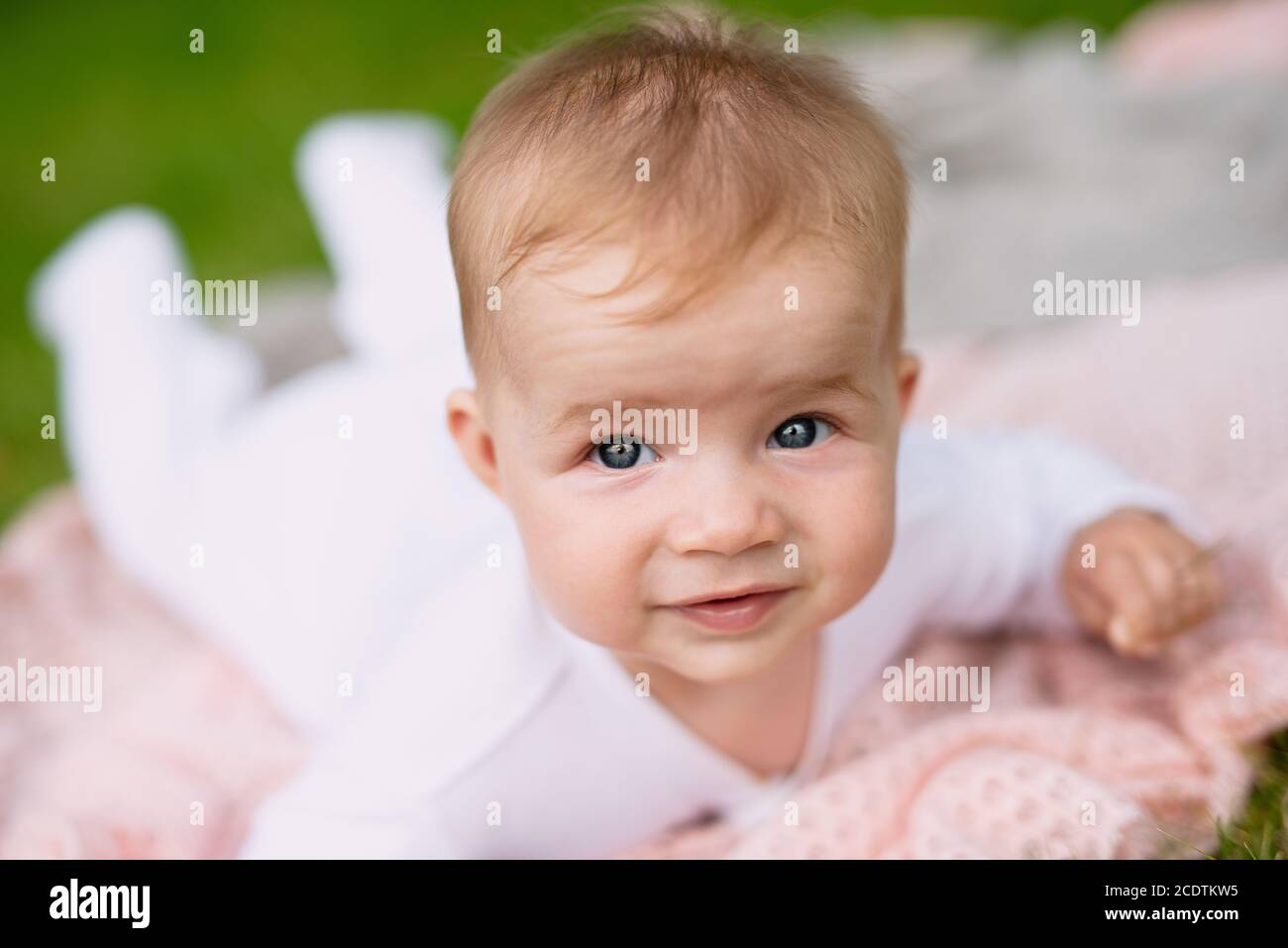 cute baby lies in  park on green grass, concept of walking outdoors, close-up of the head Stock Photo