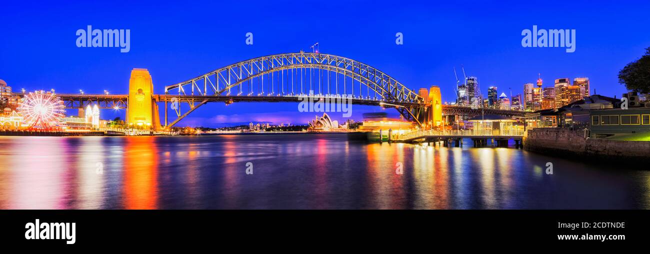 Blue sunset in Sydney city on shores of harbour around the Sydney Harbour bridge with ferry at wharf. Stock Photo