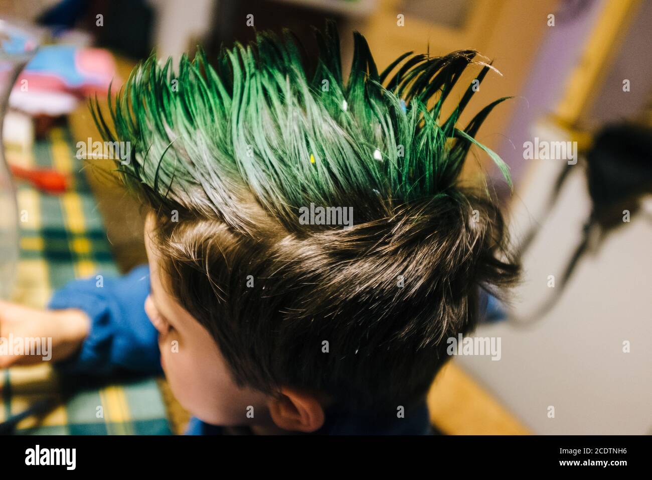 portrait of 9 year old boy at home with crest of green colored hair, performs funny gestures on the face with hands Stock Photo