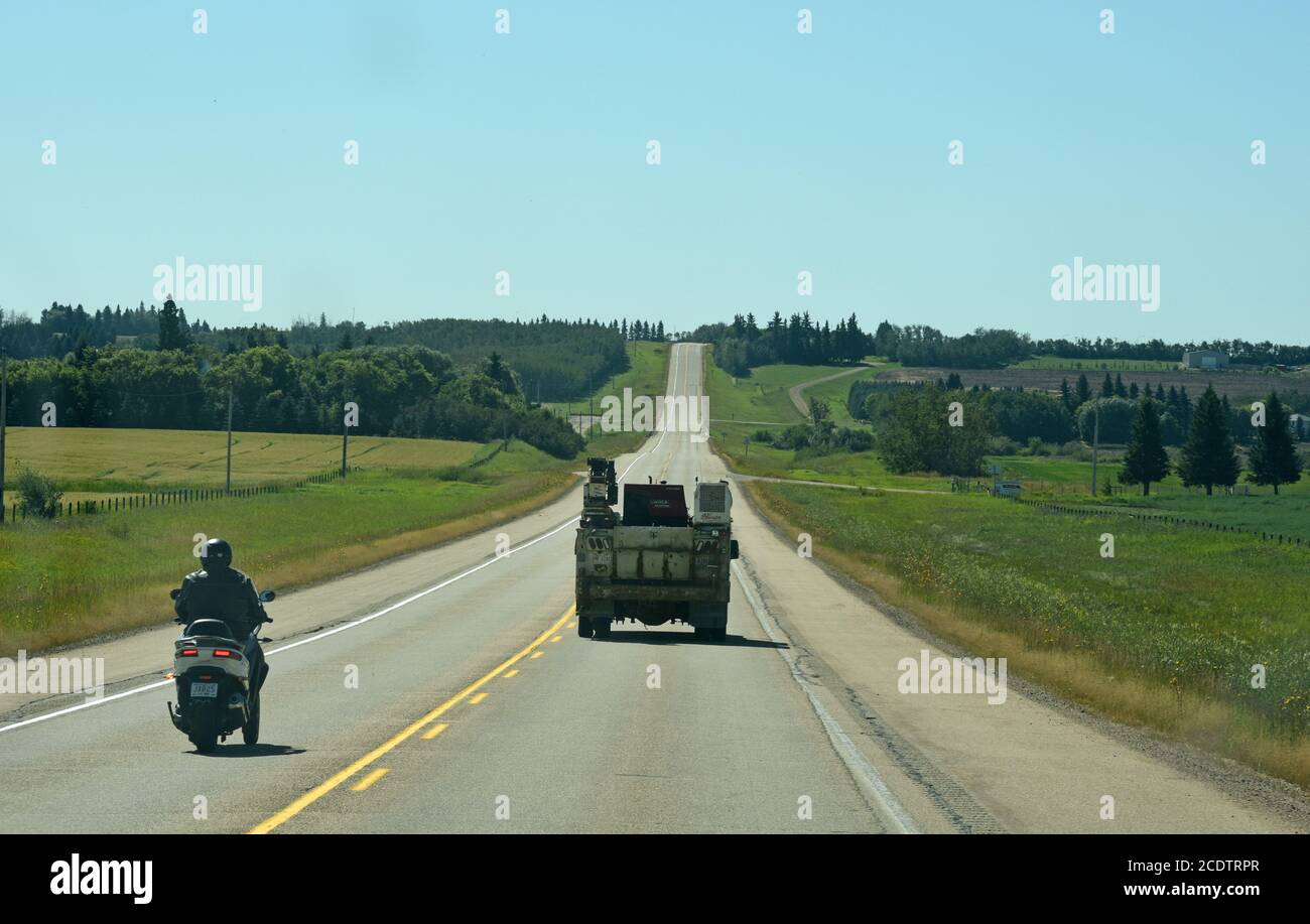 A motorcycle passes a truck on a straight stretch of country highway in central Alberta, Canada Stock Photo