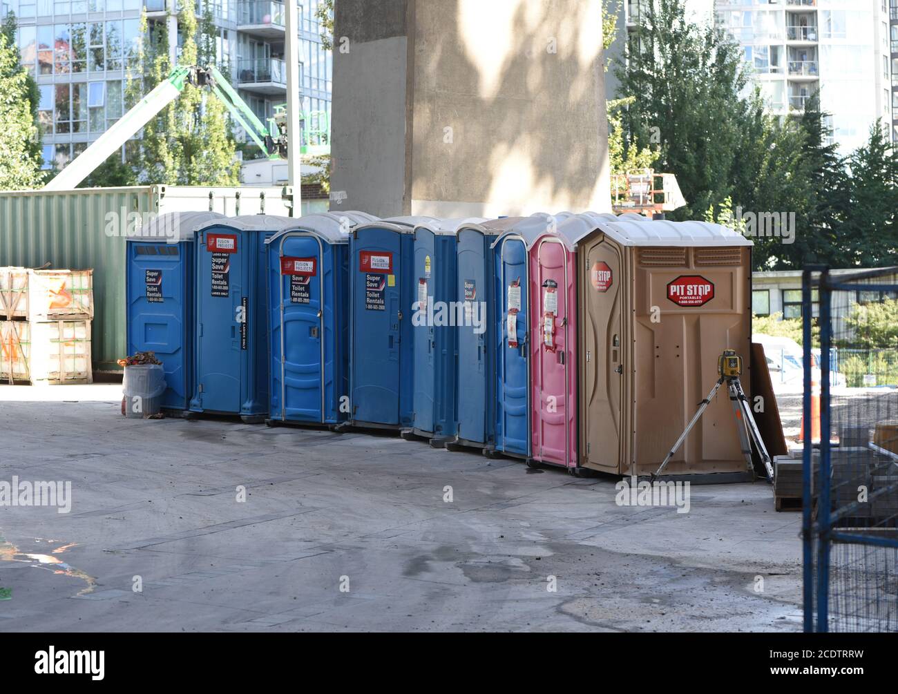 Portable toilets, blue, pink and brown, are lined up for use at a construction work site in Vancouver, British Columbia, Canada. The pink toilets are Stock Photo