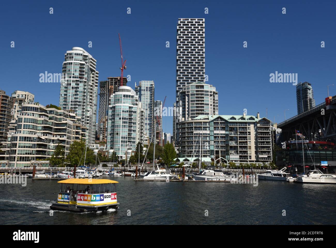 An Aquabus ferry carries foot passengers across False Creek and past downtown apartments and condominiumns on the skyline of Vancouver, British Columb Stock Photo