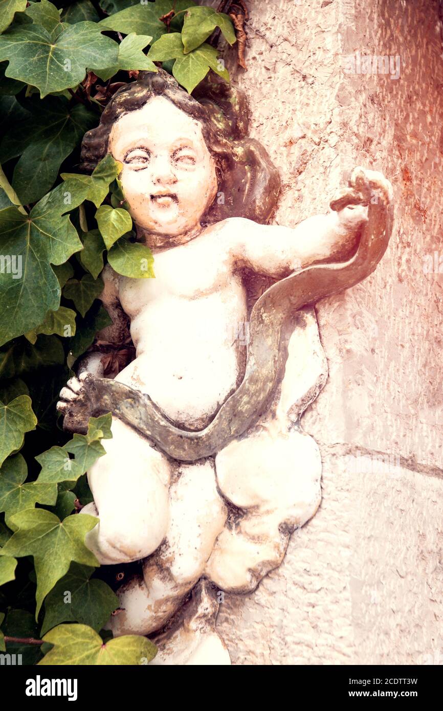 Small angel figure on house wall with green ivy on one side Stock Photo