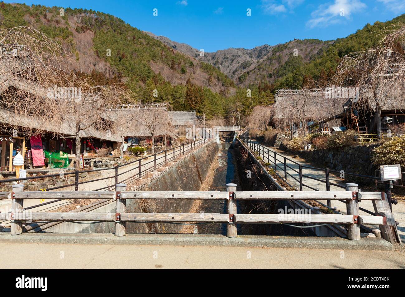 Thatched roof houses on the edge of a dry river with wooden fence in ...