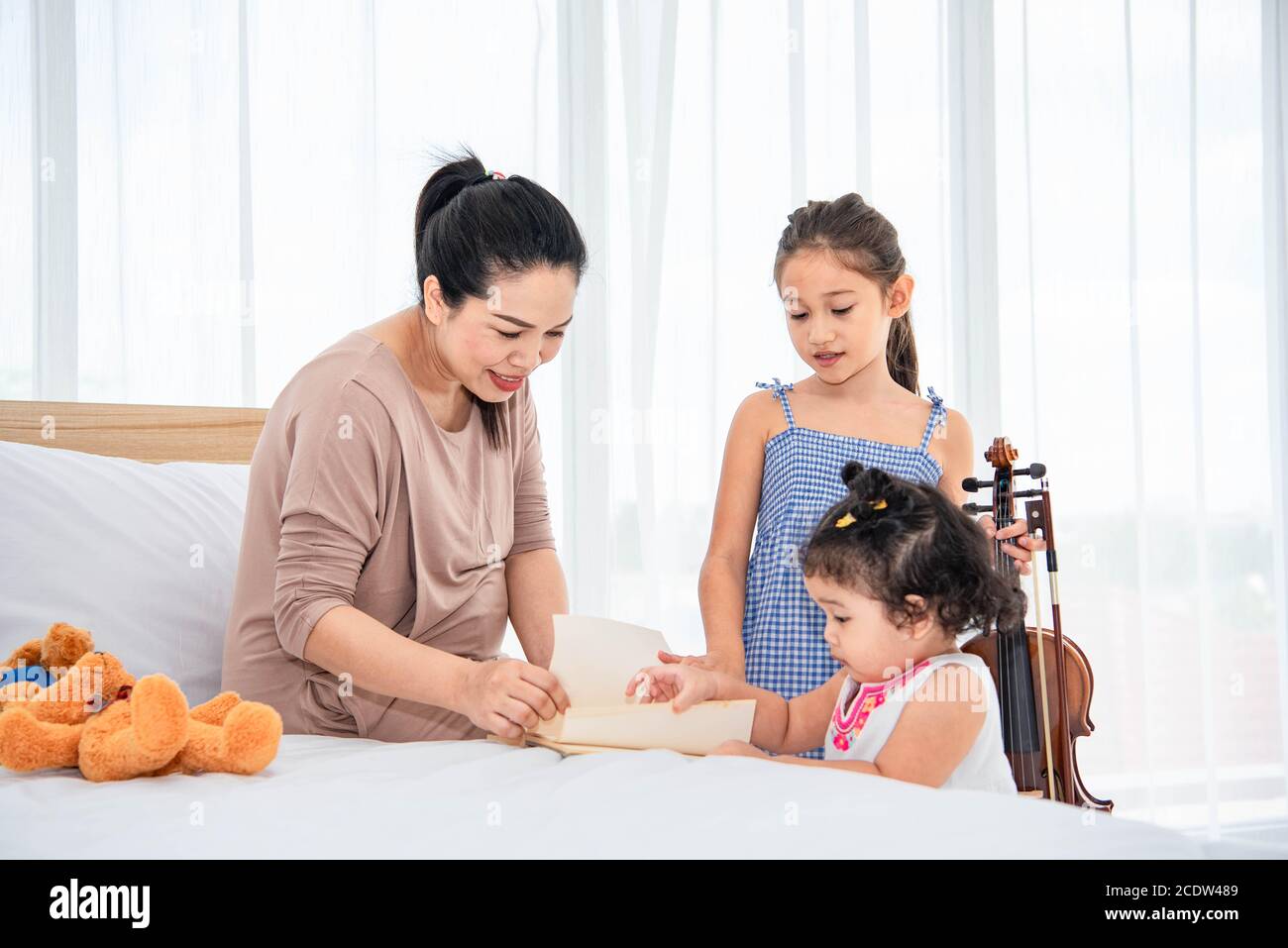 Asian mother teaching mixed raced girls daughter to reading books in their house. Quarantine in home concept. Happy family theme. Stock Photo
