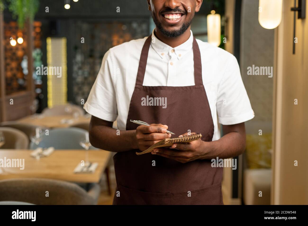 Hands of young waiter with toothy smile holding pen and small notepad Stock Photo