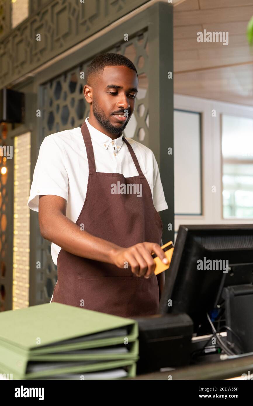 Young waiter or cashier in brown apron entering order of client in computer Stock Photo