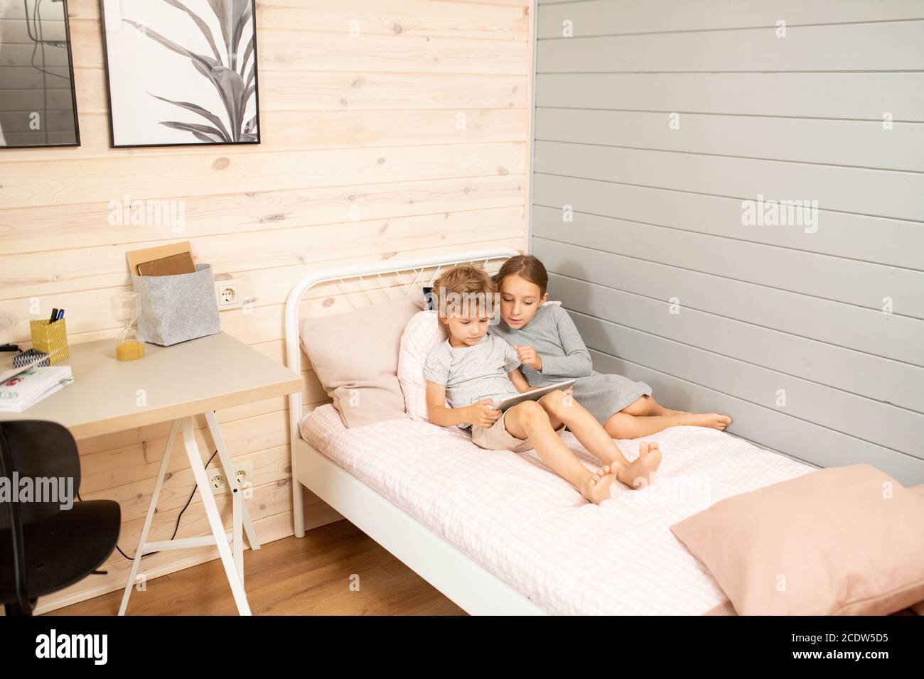 Cute little boy and his elder sister relaxing on bed and watching online  video Stock Photo - Alamy