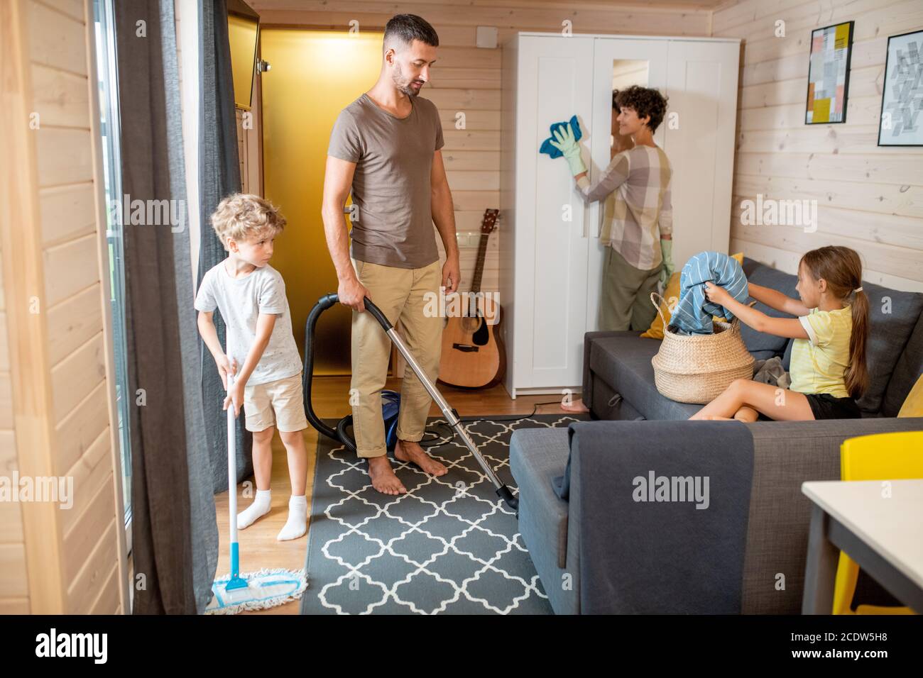 Father and son cleaning floor in living-room while mother washing wardrobe Stock Photo