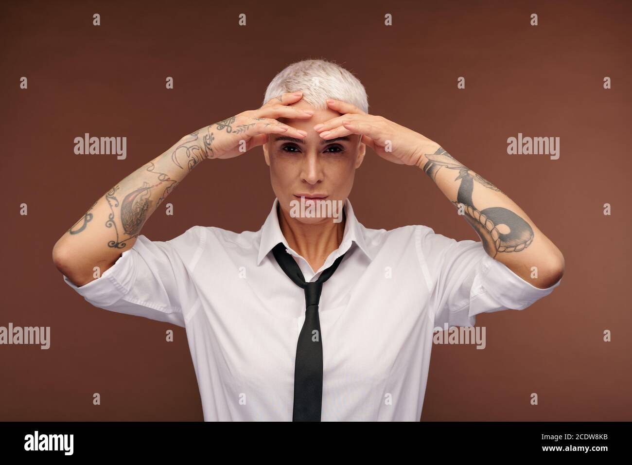 Young blond female with tattoos all over her arms keeping hands on forehead Stock Photo