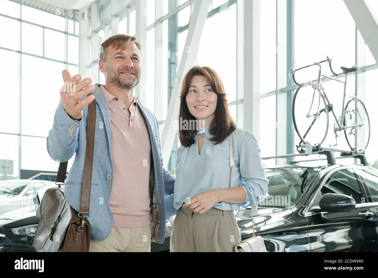 Happy mature man in smart casualwear showing his smiling wife variety of cars Stock Photo