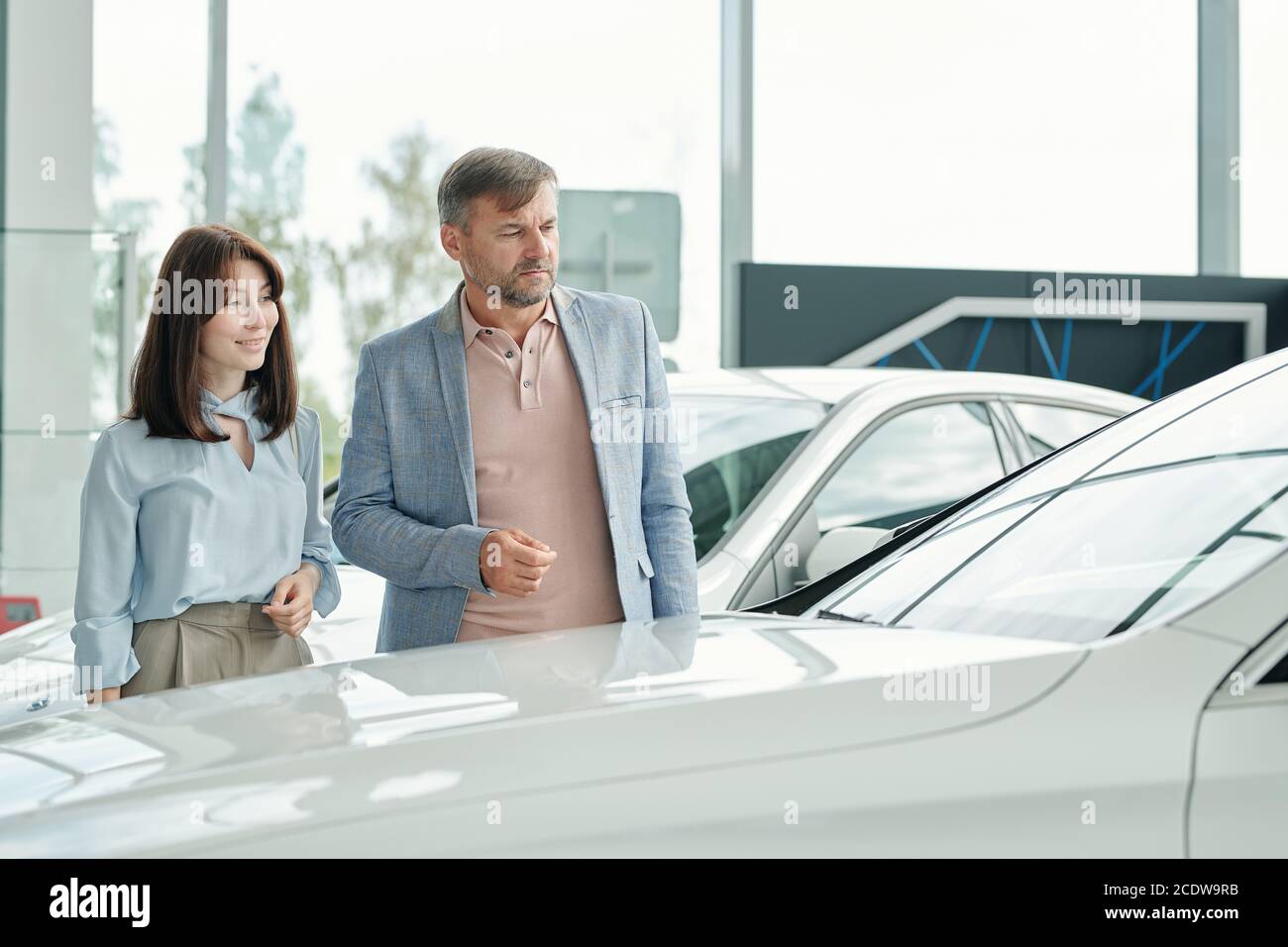 Serious mature man and his pretty elegant wife standing by new white car Stock Photo