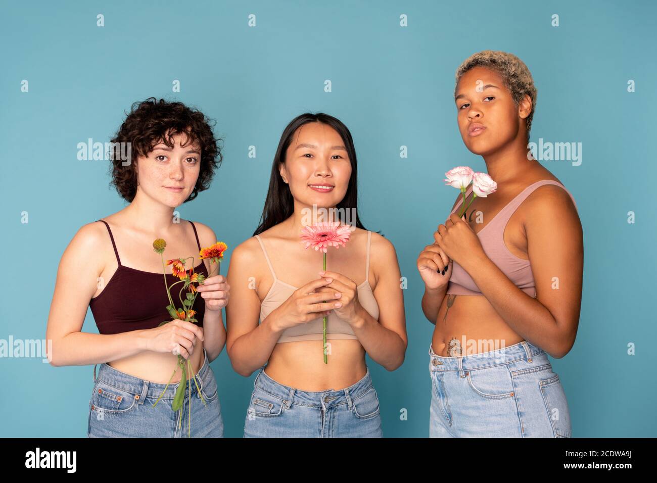 Three young pretty women in tanktops and blue jeans holding fresh flowers Stock Photo