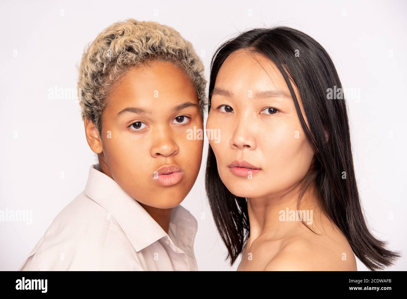 Faces of young friendly African and Asian females standing close to one another Stock Photo