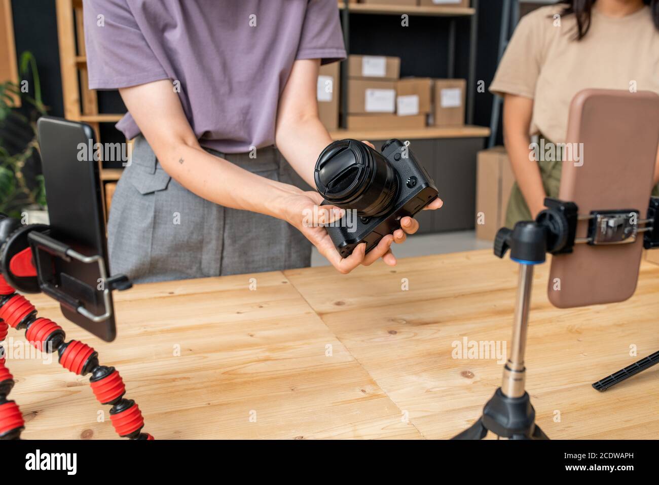 Hands of young woman in casualwear holding photocamera over wooden table Stock Photo