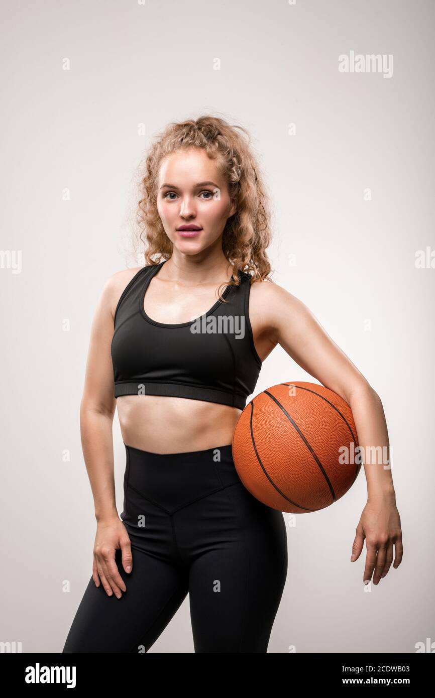 Young blond active female in sportswear holding ball between her waist and arm Stock Photo