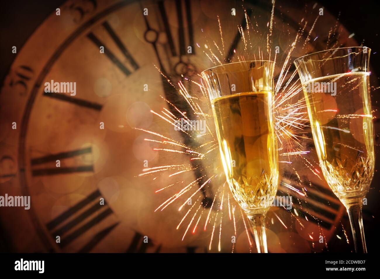 Two champagne glasses against holiday lights and clock at midnight Stock Photo