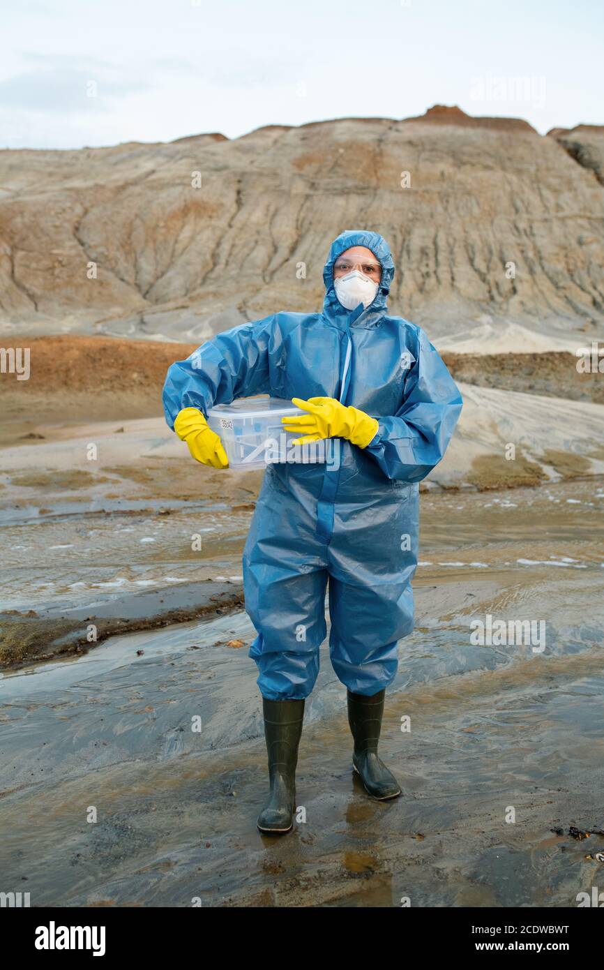 Female scientist in protective coveralls, respirator, rubber gloves and boots Stock Photo