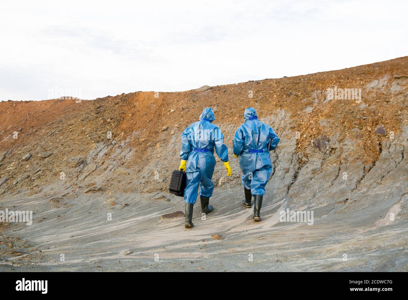 Rear view of two contemporary ecologists in protective workwear ascending hill Stock Photo