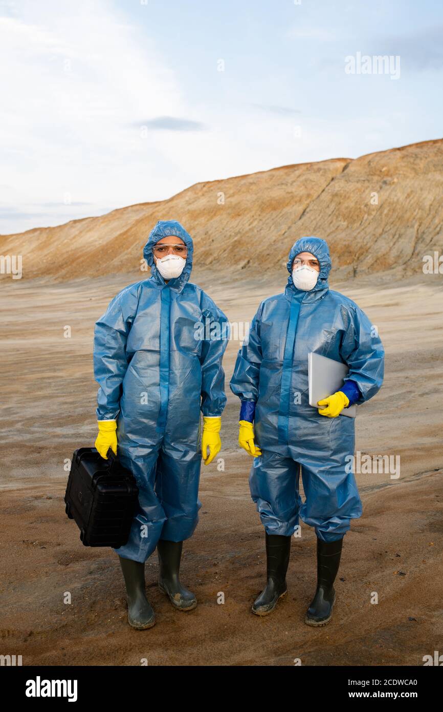Two young female researchers in protective workwear standing on polluted soil Stock Photo