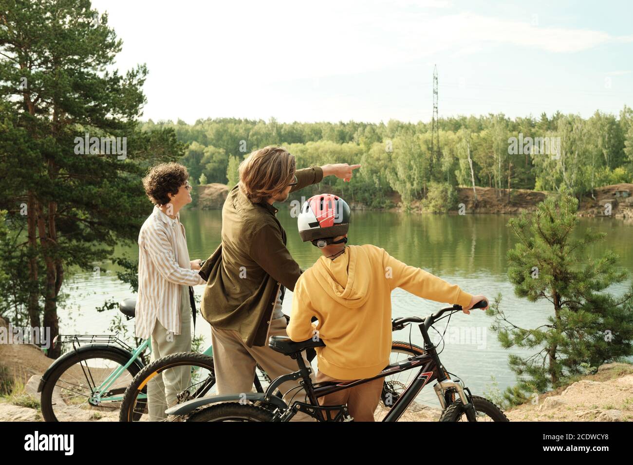 Young man pointing at opposite riverbank while talking to his son and wife Stock Photo