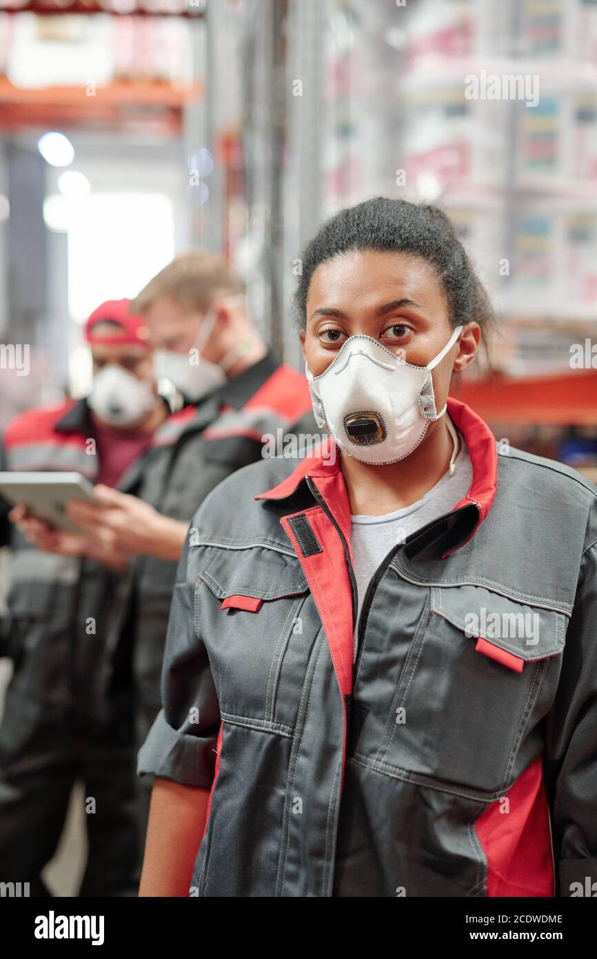 Young mixed-race woman in workwear and respirator standing in front of camera Stock Photo