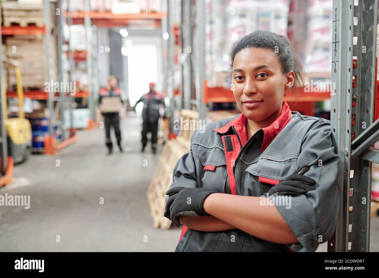 Serious young mixed-race woman in workwear and gloves crossing arms by chest Stock Photo