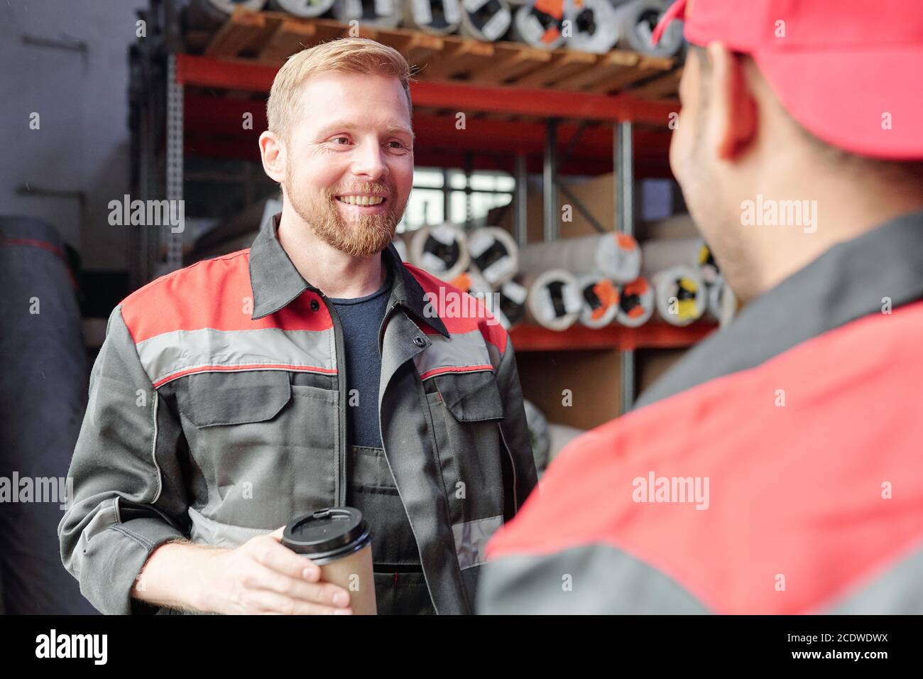 Smiling worker in uniform having coffee during conversation with colleague Stock Photo