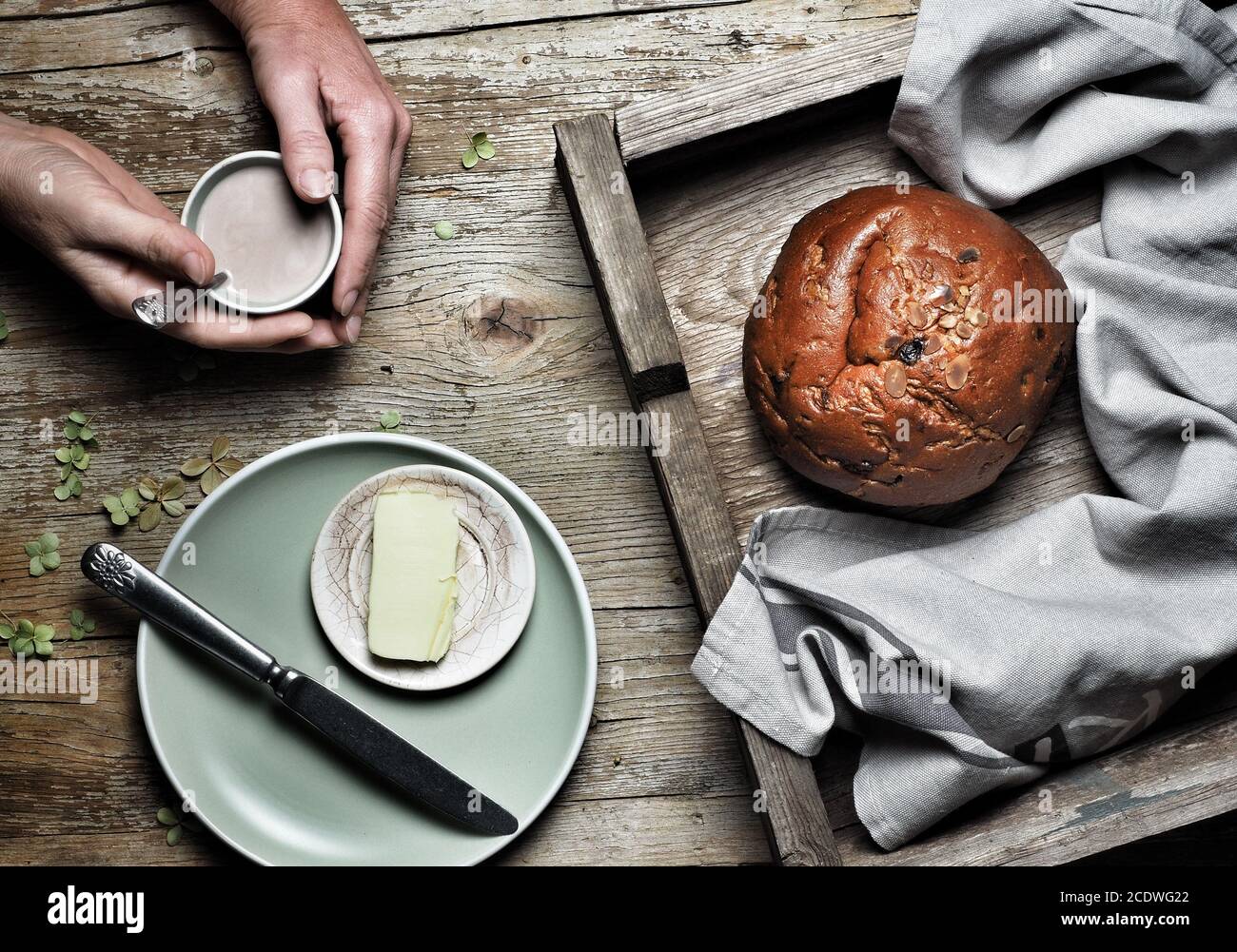Sweet bread, typical Slovak cake. A cup of cocoa milk in woman hand and piece of butter on plate on vintage wooden background. Overhead shot. Stock Photo