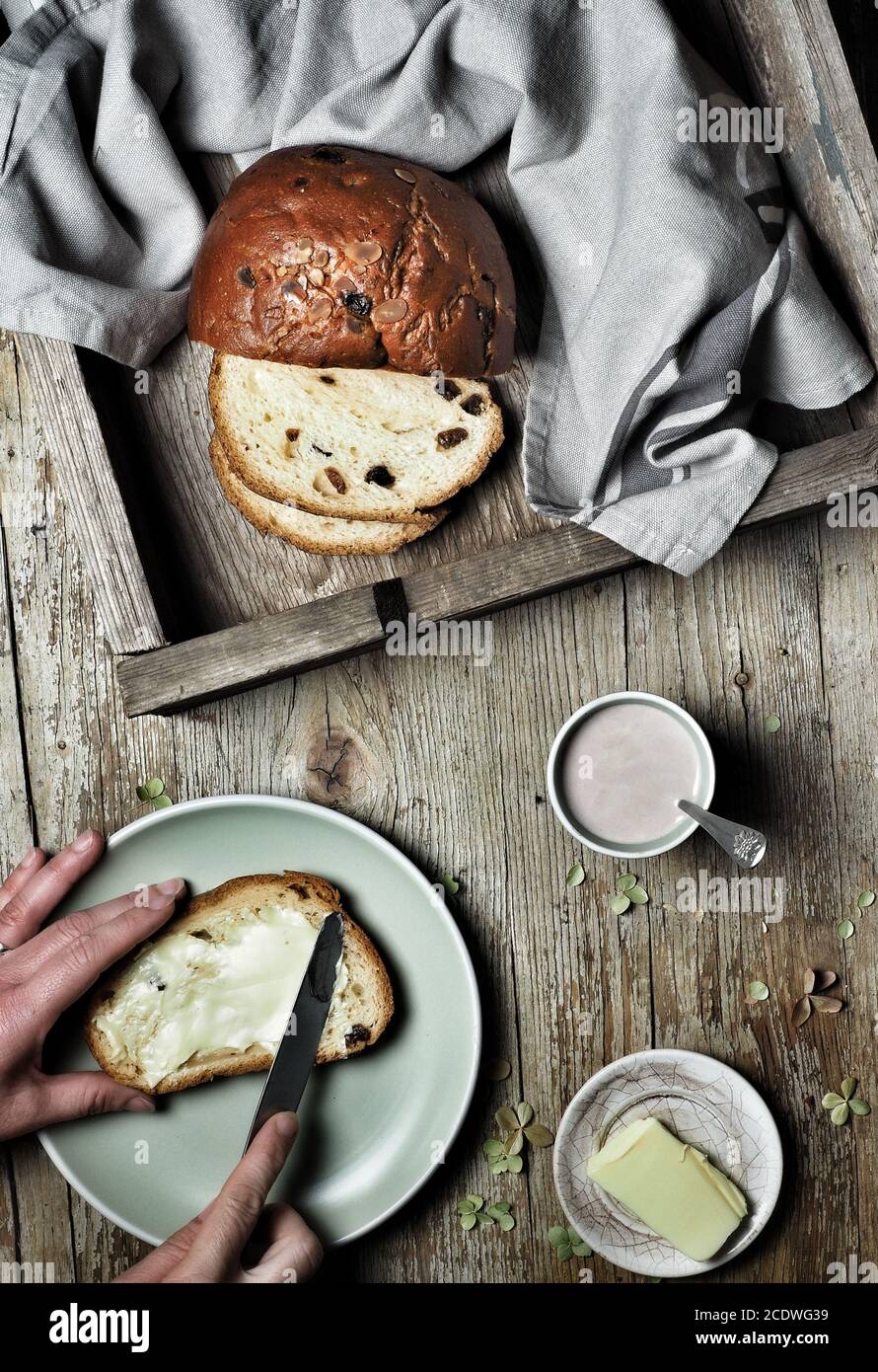 Sweet bread, typical Slovak cake. A cup of cocoa milk and woman hands spreading butter on plate. Vintage wooden background. Overhead shot. Stock Photo