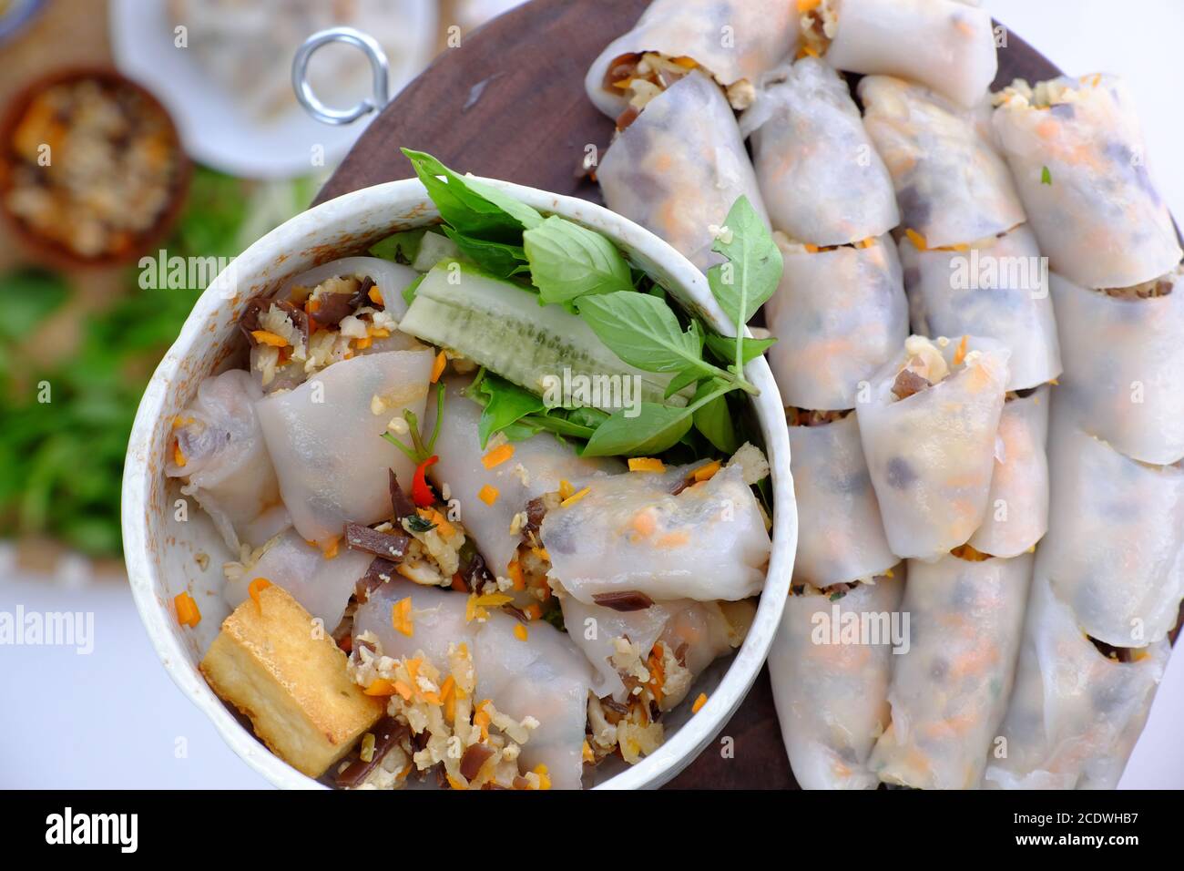 Top view people have breakfast with homemade vegan Vietnamese rice noodles roll, close up hand hold bowl of stuffed pancake dish on food background Stock Photo