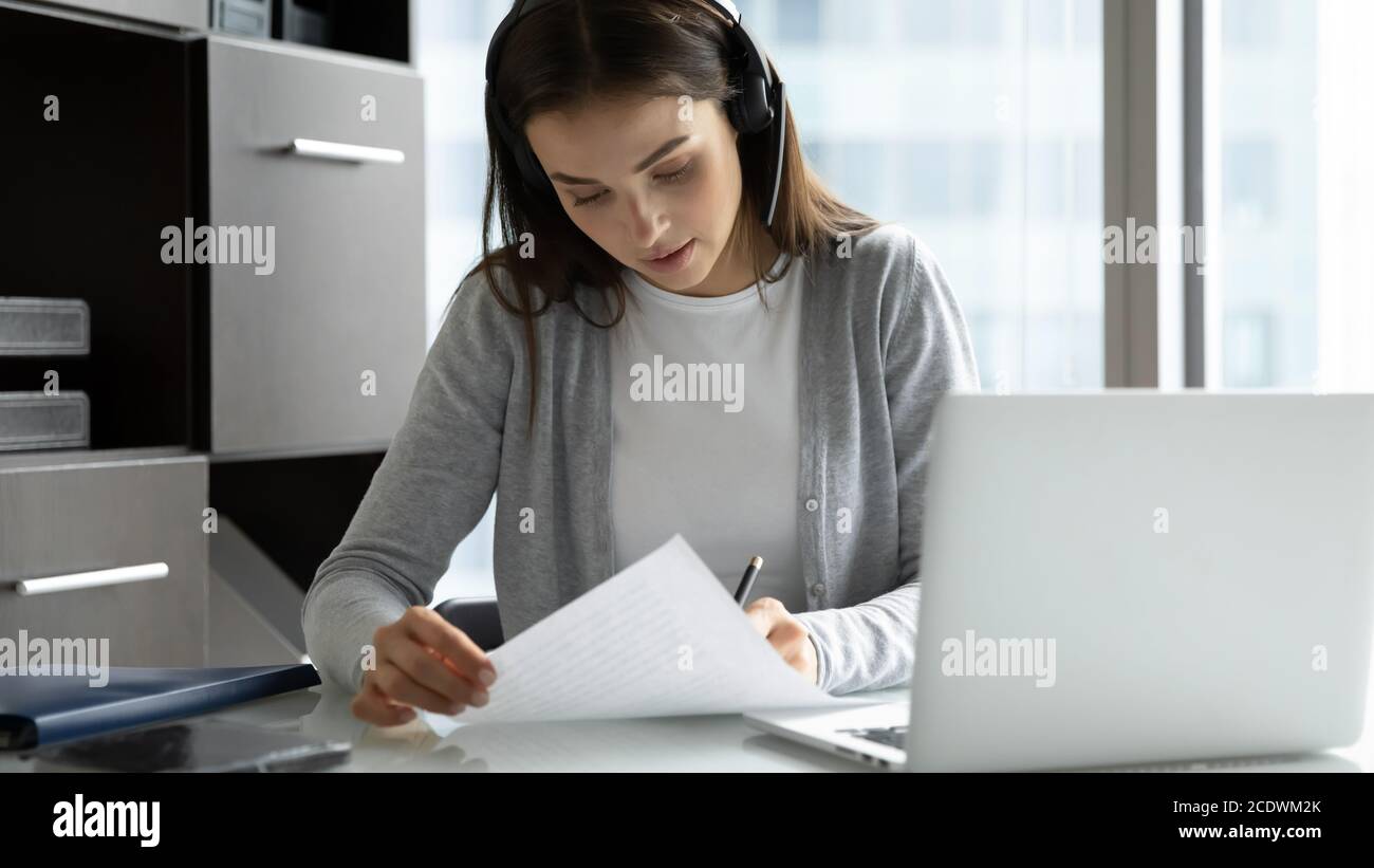 Focused businesswoman wearing headset writing notes, using laptop Stock Photo